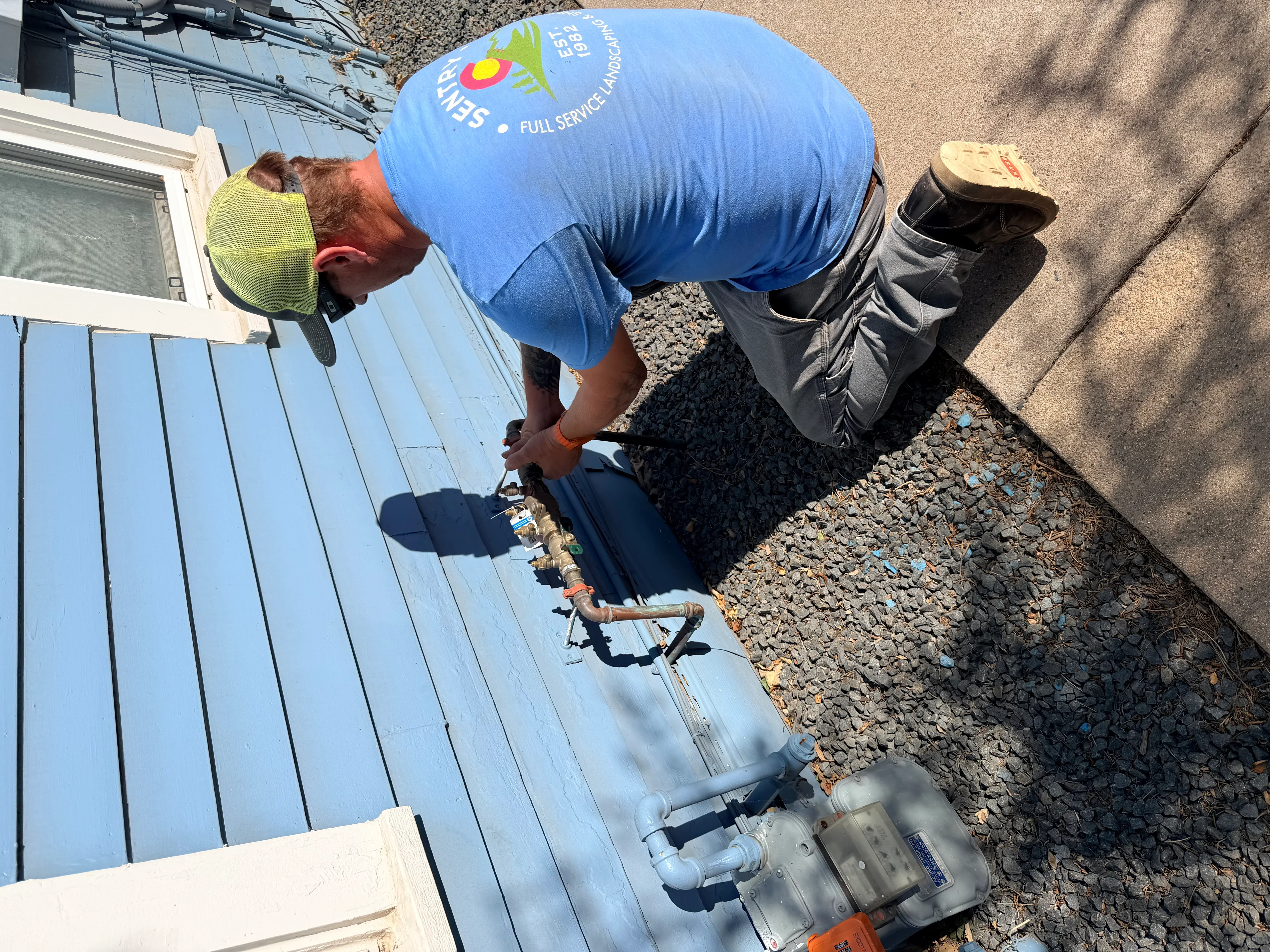 Technician installing underground irrigation pipes and valves along residential foundation