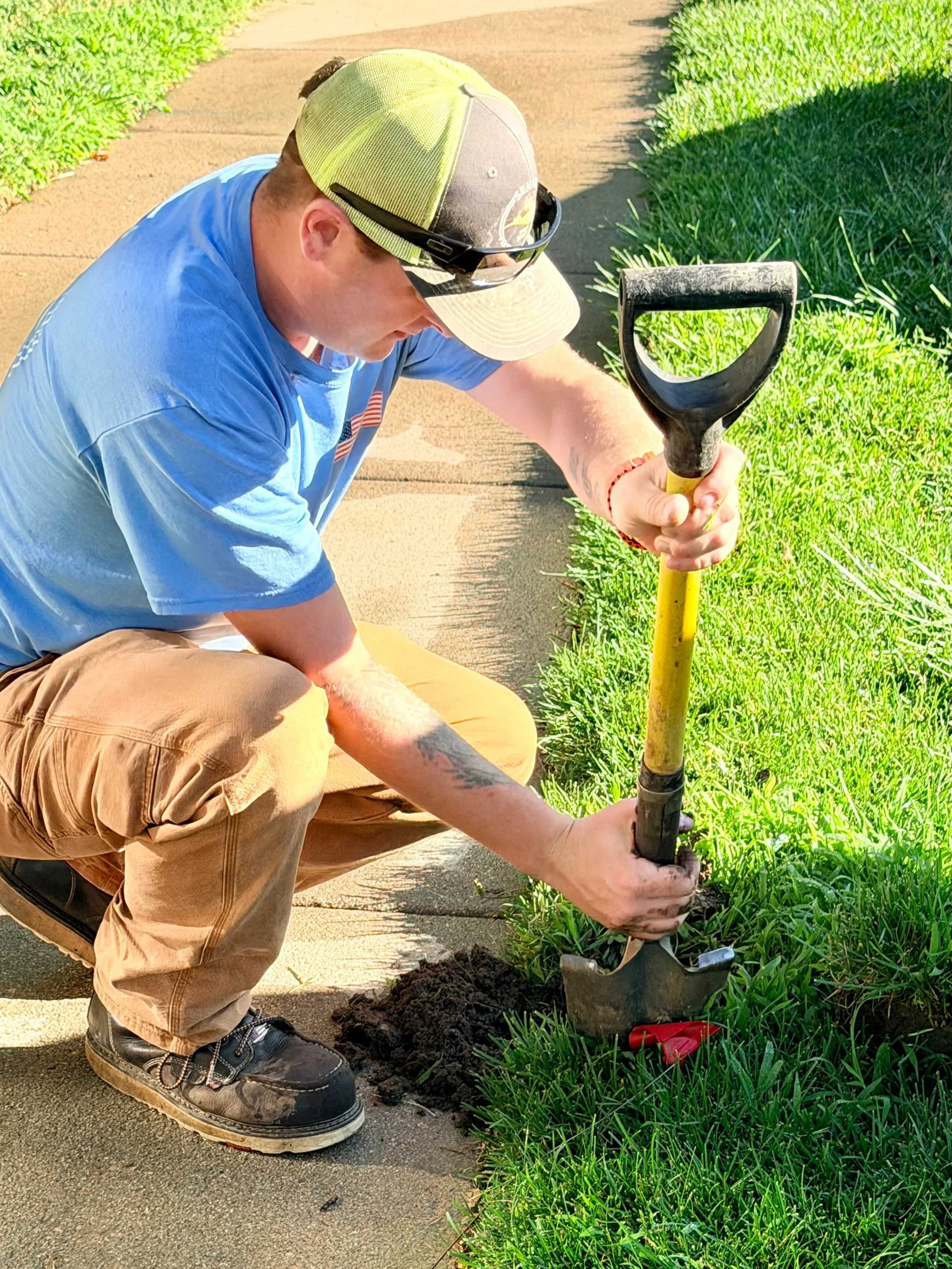 Landscaper using spade to edge lawn border along concrete walkway